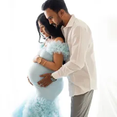 An intimate close-up of the couple, focusing on their connection as they both look down at the baby bump. The soft lighting highlights the beautiful details of the blue gown.