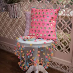 A pink cushion with mirror work and a small table with a colorful tassel tablecloth. These details are perfect for adding a touch of Indian craftsmanship to Mehendi or Diwali parties.