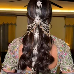 An incredibly detailed and regal half-updo, featuring a stunning piece of cascading pearl hair jewellery. This is a true showstopper look for a royal-themed wedding or reception.