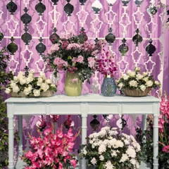 A beautiful console table arrangement with vases of pink, white, and purple flowers set against an intricate patterned backdrop.