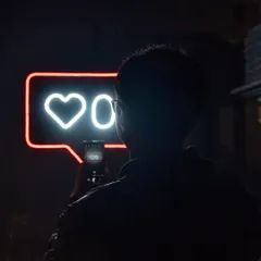 A visitor captures the neon installation on their phone, becoming part of the artwork's critique of digital life. The reflection in the phone screen adds another layer to the experience.