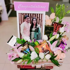 Congratulate a happy couple with this stunning floral hamper. A personalized photo frame is surrounded by a beautiful bouquet of pink lilies, roses, and various chocolates.