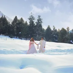 A romantic destination pre-wedding photo of a couple walking hand-in-hand through a vast, snowy landscape, capturing the scale and beauty of the location.