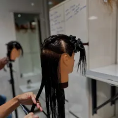 Here, a student practices creating clean, straight lines on a mannequin head. This fundamental skill is the building block for many classic haircuts, including the iconic bob.