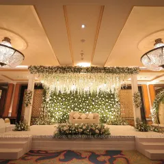 A breathtaking all-white floral stage for a Nikah reception. The design includes a lush wall of white roses, a ceiling of cascading wisterias, and elegant chandeliers, creating a scene of pure opulence.