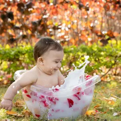 The perfect end to a fun day. A happy baby splashes in a milk bath with rose petals, set against a beautiful autumn-colored background.