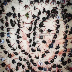 A closer top-down image of a Muharram ritual, focusing on the abstract patterns created by the participants. The stark contrast of black clothing against the ground creates a powerful and emotional visual story of faith and remembrance.