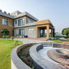 The rear of the Sonipat farmhouse, featuring a covered veranda and a custom-designed circular fire pit area that serves as a focal point for the landscape.