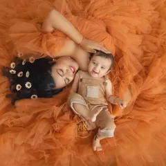 An aerial view of a mother and her smiling baby lying together on a sea of orange tulle, creating a warm and joyful image.
