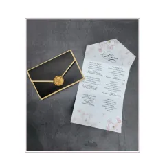 An elegant menu card designed to look like a sealed letter. The floral-printed menu is held within a black and gold laser-cut sleeve, complete with a faux wax seal.