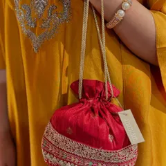 A classic red potli with a delicate silver embroidered border, held against a mustard yellow kurta. It's the perfect accessory to add a festive touch.