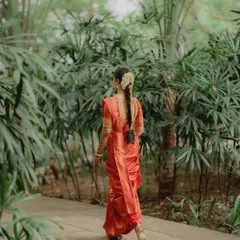 A view of the traditional South Indian braided hairstyle, beautifully decorated with flowers, walking away into a lush green background.
