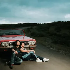 A cool, relaxed portrait of a couple sitting on the road with a vintage red convertible. This shot has a classic, romantic road trip vibe, perfect for a fun and adventurous pre-wedding theme.