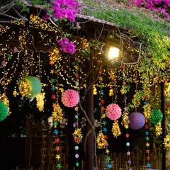 An evening view of the colorful hanging decor, illuminated by fairy lights. The bougainvillea flowers on the roof add another layer of natural beauty to the festive setup.