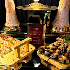 A beautifully arranged sushi station featuring a variety of rolls and nigiri. The menu clearly lists options like Teriyaki Chicken Katsu and Asparagus Tempura, served on traditional wooden displays.