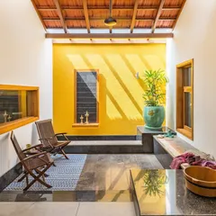 A sunlit courtyard nook brings warmth and life into the home. The vibrant yellow wall, terracotta tile roof, and the play of shadows from the skylight create a space that feels both traditional and refreshingly modern, perfect for a quiet morning.