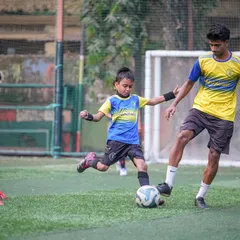 A coach gently guides a very young player during a drill, demonstrating a tackle. This heartwarming shot shows our commitment to helping our youngest players fall in love with the game.