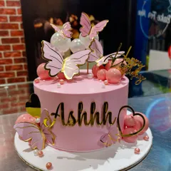 A chic pink cake decorated with golden butterflies and pink spheres. The custom gold name adds a personalized and modern touch to this stylish design.