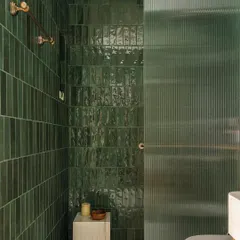 The bathroom in Apartment 1005 is a study in texture and color. We used handmade green ceramic tiles to create a rich, vibrant shower enclosure, contrasted with a fluted glass door that plays with light and transparency.