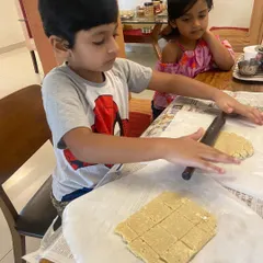 At-home learning continues with practical life skills. Here, a child is rolling out dough for a sweet treat, practicing the coordination and strength needed for many other academic and life activities.