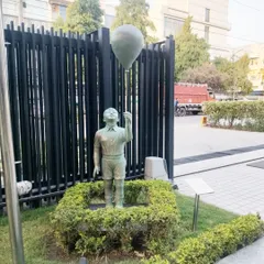A charming life-size sculpture of a young boy holding a balloon, installed in a garden in Gurgaon. The piece has a classic weathered bronze finish.