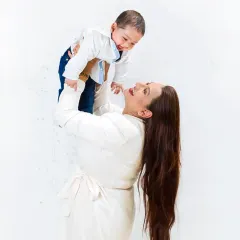 A mother joyfully lifts her baby into the air, both sharing a moment of pure happiness. This candid shot captures the dynamic and loving bond between a mother and her child.