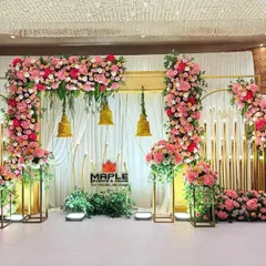 A beautiful blend of gold structures and pink floral arrangements for a romantic wedding stage. The hanging temple bells and warm lighting add a traditional touch to this elegant and modern setup.
