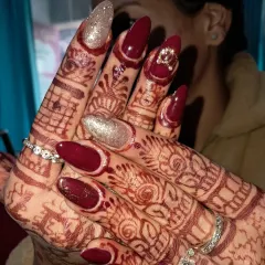 We love how these bridal nails look with the intricate mehndi design. This set features a deep maroon polish on long almond nails, with two accent nails in a sparkling champagne glitter and a small bow charm.