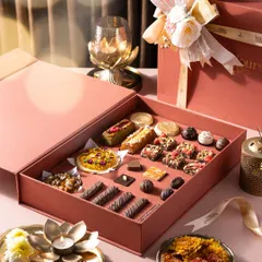 An open view of a luxurious pink gift box, revealing an assortment of handcrafted Belgian pralines, financier bars, mini tarts, and other bite-sized desserts. This gives a close-up look at the intricate and diverse patisserie I create for the festive season.