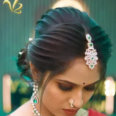 This image highlights the elegant hairstyle created for the reception look. A textured, twisted bun is adorned with a diamond and emerald maang tikka, showcasing how hairstyling is a crucial element of the total look curation I provide.