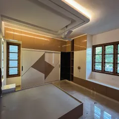 This bedroom design features a stylish wardrobe with a geometric pattern on the sliding shutters. The combination of glossy beige and brown laminates, along with a bay window seating area, creates a multipurpose and aesthetic space.