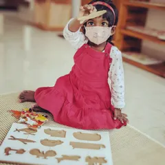 A child proudly holds up a piece from a wooden puzzle. Puzzles like these help develop problem-solving skills, shape recognition, and fine motor control.