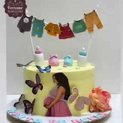 A sweet baby shower cake with a clothesline of baby clothes as a topper. This mixed fruit cake is decorated with butterflies and a beautiful image of a pregnant mother.
