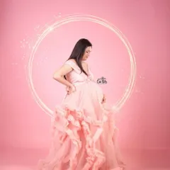 A touch of sparkle for a magical moment. This shot highlights the beautiful silhouette of the pink ruffled gown, perfect for capturing that pregnancy glow in the studio.