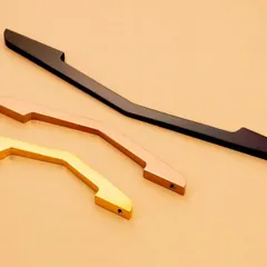 Three elegantly curved handles in different metallic finishes. The minimalist composition emphasizes their unique shape and form.