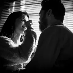 A playful and loving moment between a couple, captured in beautiful black and white. The light from the window blinds creates a lovely pattern, adding texture and mood to this candid shot.