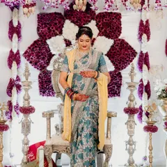 A portrait of the mother-to-be, glowing in front of a custom-designed floral backdrop. The combination of deep purple and white flowers with traditional hanging elements provides a regal and elegant setting for her special day.