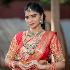 A beautiful bride wearing a Victorian-style necklace with green stones. The antique finish looks stunning against her red and orange saree.