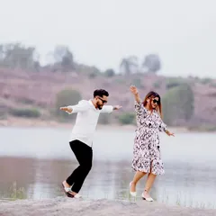 A playful, candid shot of a couple balancing on a rock by a lake. This image captures a fun, unscripted moment during their outdoor adventure shoot.