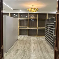 An entrance view of a grand walk-in closet under construction. The scale of the space is immediately apparent, with extensive custom shelving and a statement chandelier promising a truly luxurious final result.