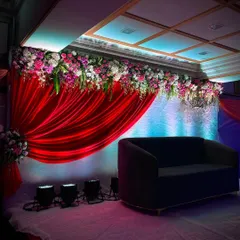 Another view of the red-draped reception stage, showing how the lighting and floral arrangements come together. The combination of lush flowers and dramatic lighting creates a perfect backdrop for wedding photos.