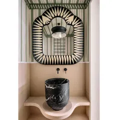 We amped up the whimsy in this Eden House powder room with a custom-shaped mirror from Scarlet Splendour, a freestanding black marble sink, and vibrant, illustrative wallpaper.