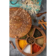 A top-down shot of a beautifully carved wooden spice box. The frame is filled with colorful spices like turmeric and chili powder, along with whole spices like star anise, creating a rich and aromatic scene.