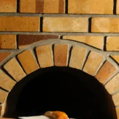 A pizza being carefully removed from our brick wood-fired oven. This traditional cooking method is key to achieving the perfect crispy crust and smoky flavour.