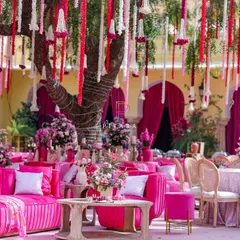 We created a vibrant outdoor lounge with plush fuchsia velvet sofas and elegant seating arrangements. Floral garlands hanging from the tree above added a touch of traditional charm to this modern, colorful setup.