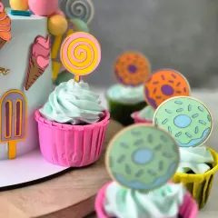 A closer look at the matching cupcakes for the Candy Land theme. Each one is topped with light whipped cream frosting and a cute, edible topper like a lollipop or donut.