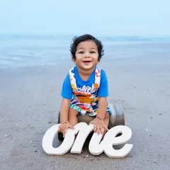 A happy one-year-old boy poses with a "one" sign during his beach birthday photoshoot.