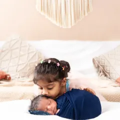 A sweet moment between siblings, as the older sister gently kisses her newborn brother's head.