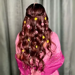 A detailed shot of the floral half-updo. The combination of yellow and pink flowers with pearls cascading through the brown wavy hair creates a beautiful, fresh look.