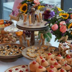 A vibrant and colorful spread designed for a celebratory gathering. This table features a beautiful floral arrangement alongside my signature truffle cigar rolls and an array of savory tarts.